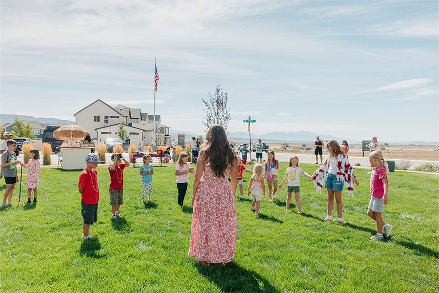 A group of kids and an activities director standing in a circle in a green grass field in the Firefly community in Eagle Mountain, Utah