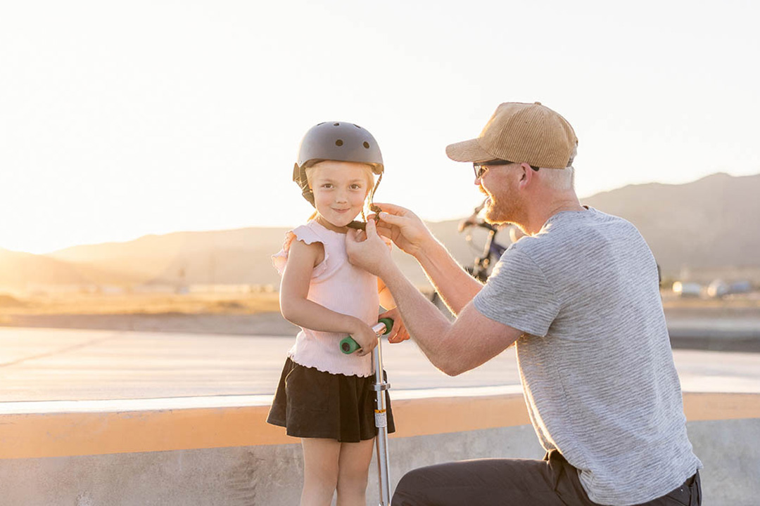 A Father helping his young daughter put on a helmet at the Firefly Skatepark in Eagle Mountain, Utah